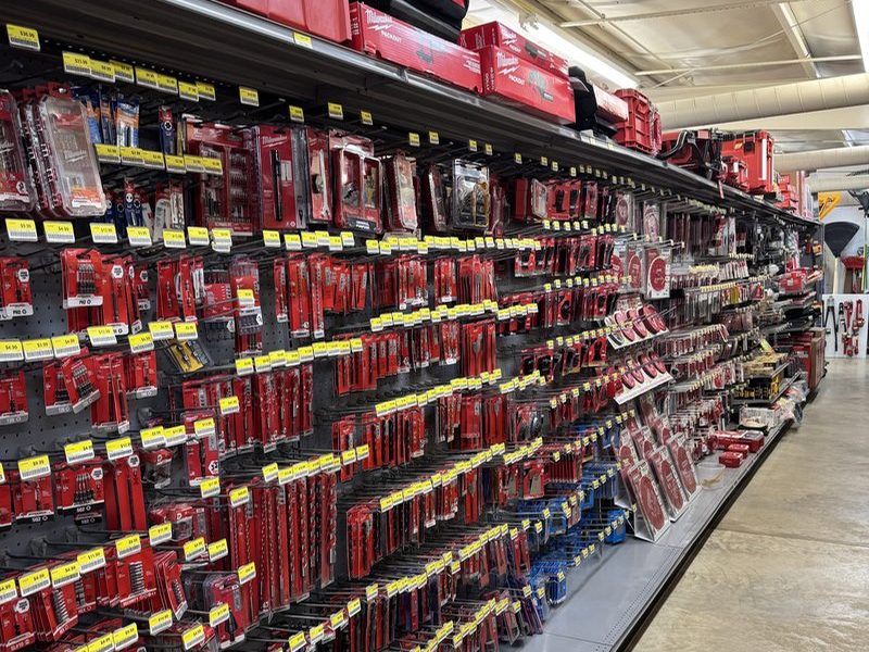 A long tool aisle hung with red Milwaukee accessories on pegboard, with red tool cases on the top shelf